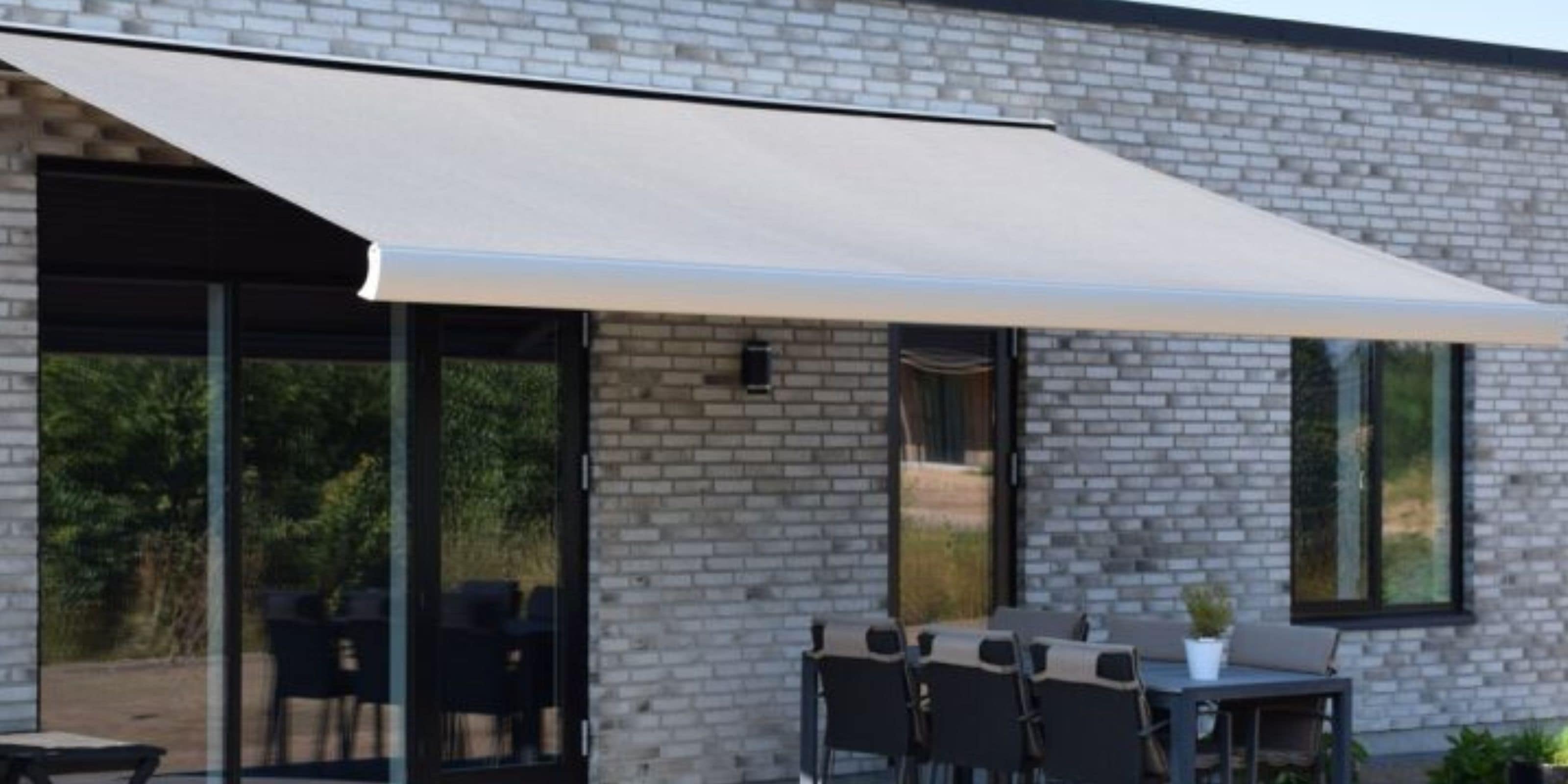 Kassettemarkise i beige monteret over terrasse med udendørs spisemøbler ved moderne murstenshus